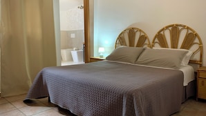 Un lit bien fait, avec une couvre-lit matelassé, une tête de lit en bois et une table de chevet surmontée d’une lampe.