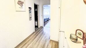Un passadís amb un quadre emmarcatetjat amb la inscripció 'SIEGBURG' a la paret, una porta que dona a una habitació i una vista d'un balcó amb barana.