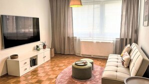 Un saló amb televisió de pantalla plana, un sofà, una taula de centre i una finestra amb cortines.