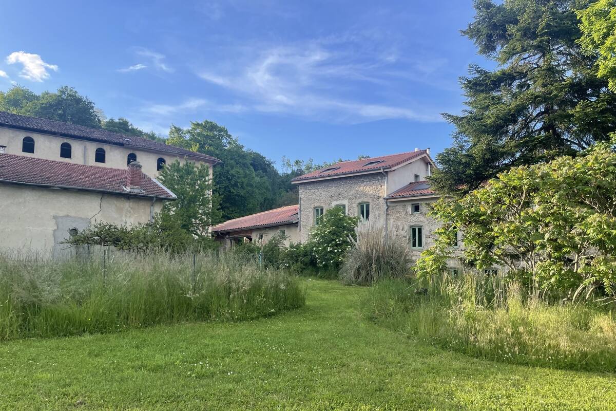 A rural setting with stone buildings, a grassy path, and dense greenery.