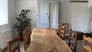 A dining room with a long wooden table, six wooden chairs, a potted plant, a light blue door, and a hanging pendant light. - Fabrique des Luddites - chambres et gîte (Chatte)