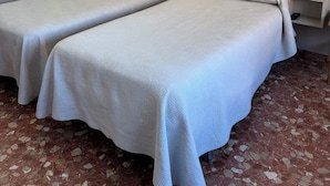 Une chambre d’hôtel avec deux lits simples, une petite table de chevet avec une lampe, une prise électrique et une étagère avec un téléphone.