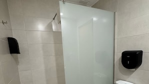 Une salle de bain moderne avec une douche à parois de verre, des toilettes et un distributeur de serviettes en papier.