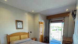 Une chambre à coucher avec un lit, une tête de lit en bois, une table de chevet, un tableau encadré au mur et un balcon avec vue.