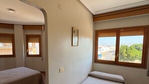 Une chambre avec deux lits, une petite table et une fenêtre donnant sur des immeubles et des arbres.