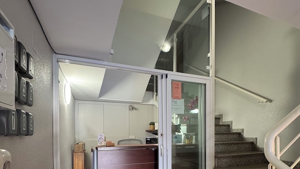Un intérieur moderne avec un escalier, un bureau en bois et une porte en verre donnant sur une autre pièce.