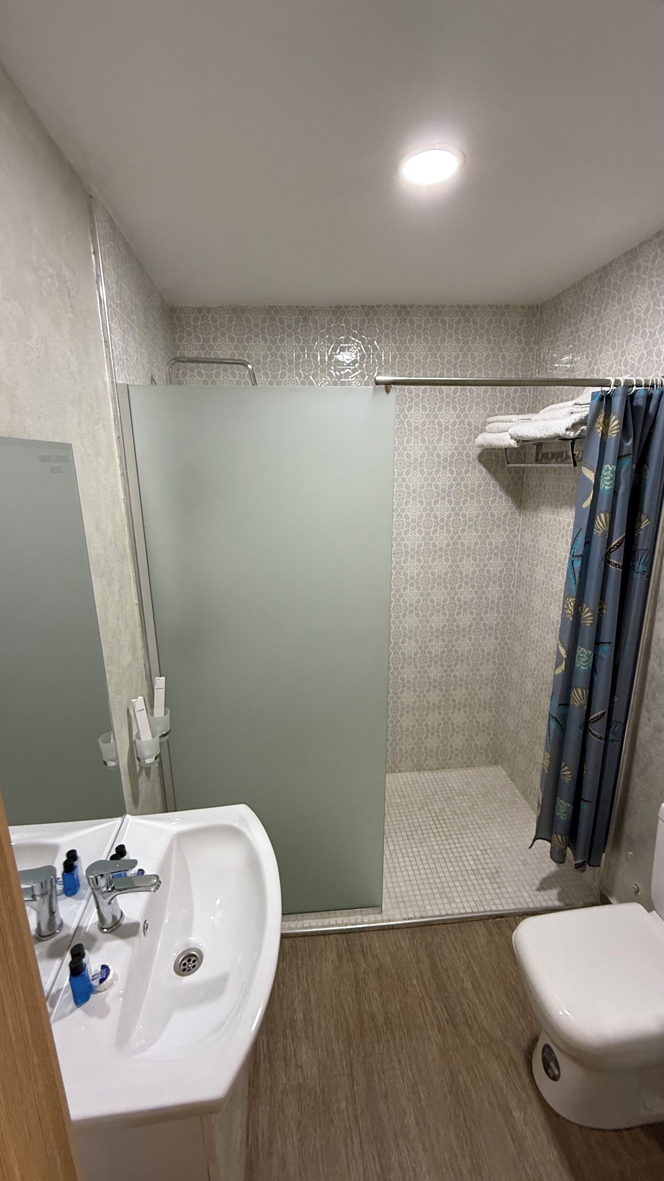 A bathroom with a shower, toilet, sink, and a mirror.