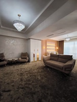 A modern living room with a large beige sofa, two armchairs, a small round table, and a large window with curtains.