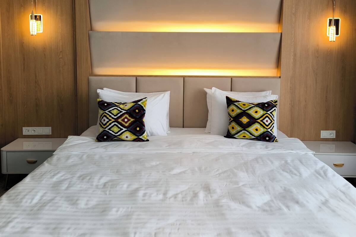 A hotel room with a large bed, two nightstands, a wooden headboard, and wall-mounted lighting.