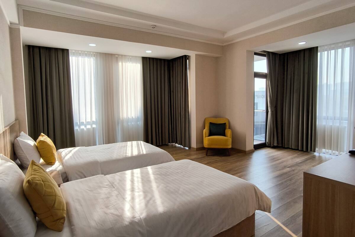 A hotel room with two beds, a desk, and a yellow armchair.