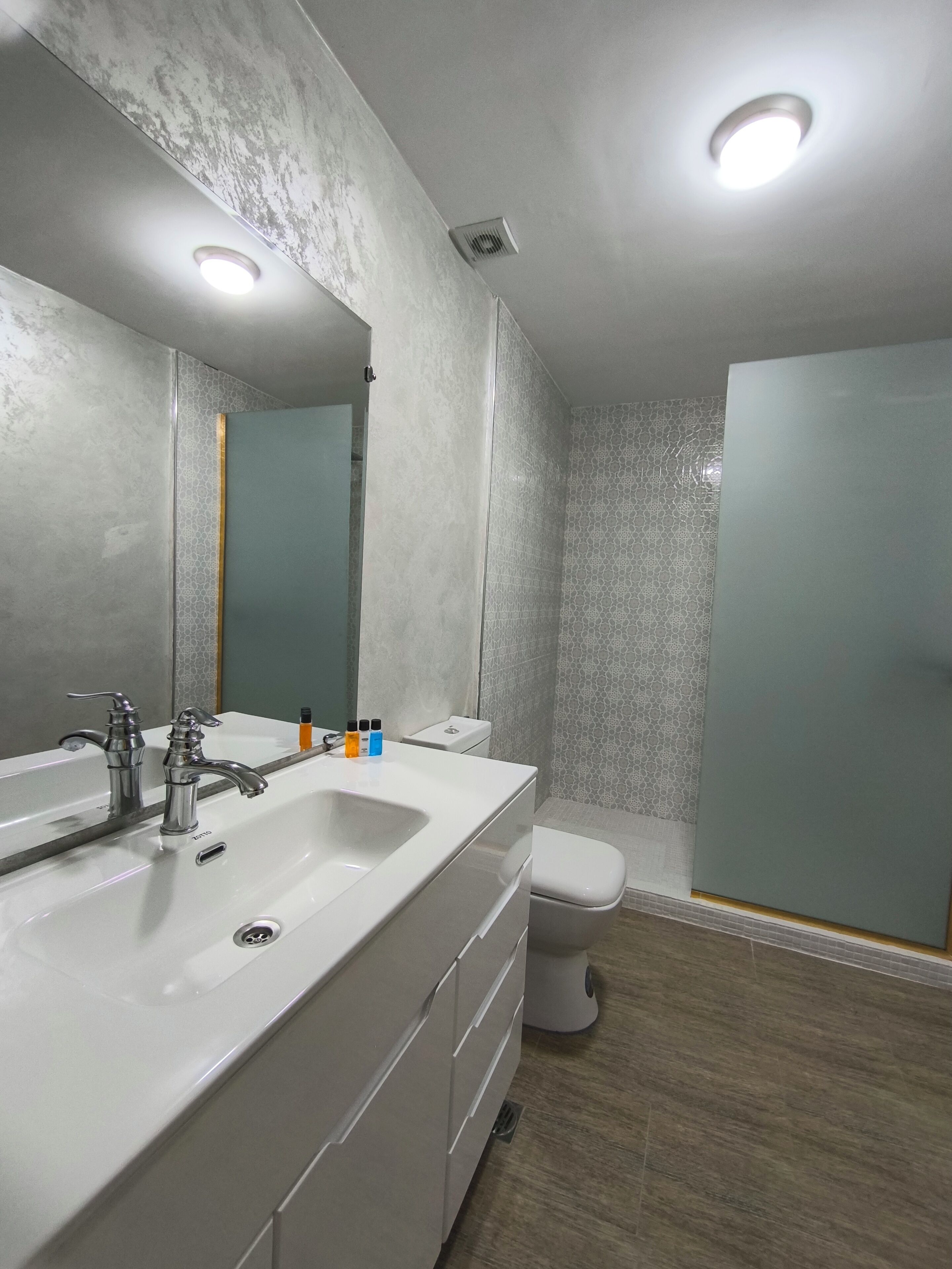Een moderne badkamer met een grote spiegel, twee wastafels, toilet en een douche.
