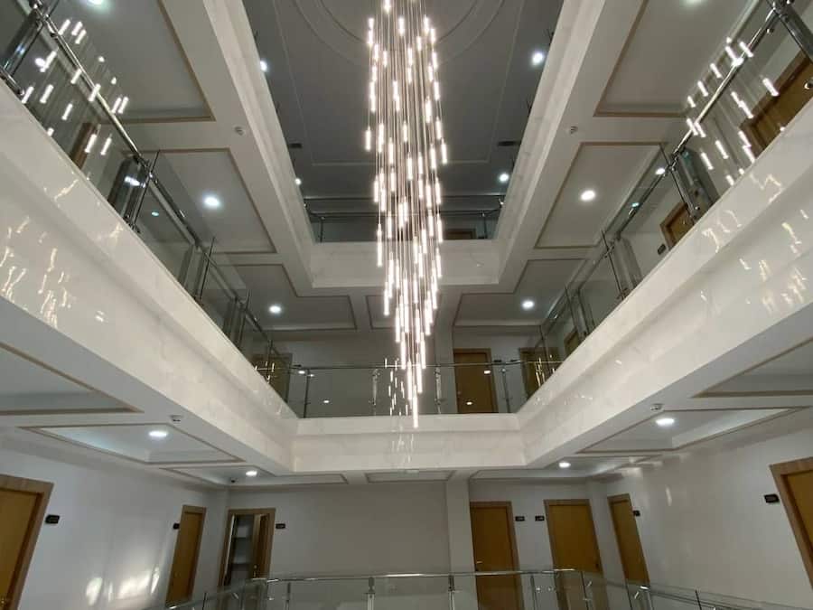 Um átrio com vários níveis, um lustre central, guarda-corpos de vidro e um design simétrico.