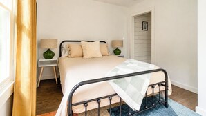 Une chambre à coucher avec un lit, des tables de chevet, des lampes, une fenêtre avec des rideaux et une porte.