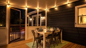 Un espace extérieur aménagé pour les repas, avec une terrasse en bois, une table dressée pour quatre personnes et des guirlandes lumineuses.