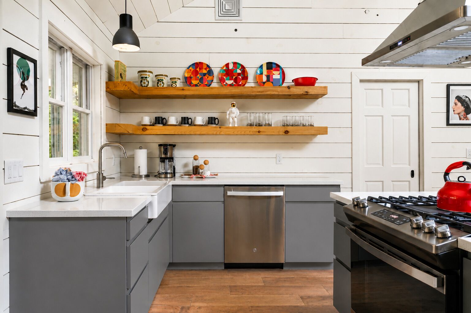A modern kitchen with grey cabinets, a stainless steel dishwasher, a red kettle, and a gas stove.