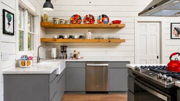 A modern kitchen with grey cabinets, a stainless steel dishwasher, a red kettle, and a gas stove.
