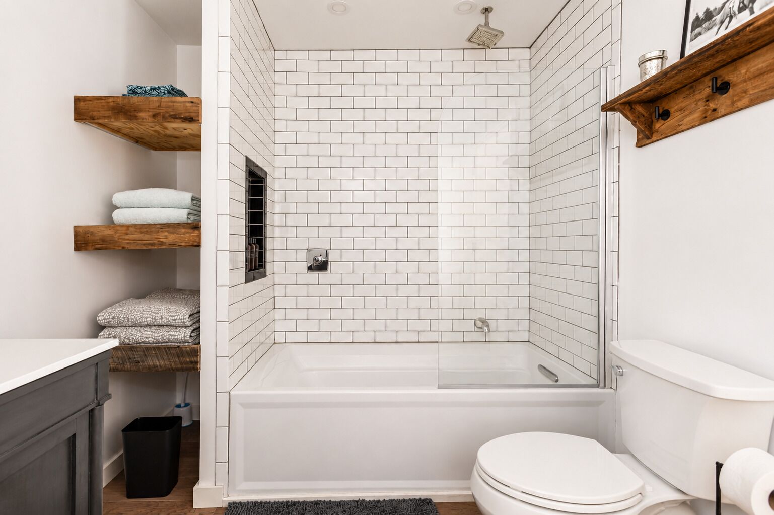 A modern bathroom with white subway tiles, a freestanding bathtub, a toilet, and wooden shelves with towels.
