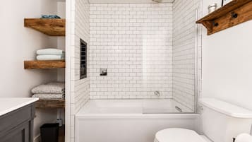 A modern bathroom with white subway tiles, a freestanding bathtub, a toilet, and wooden shelves with towels.