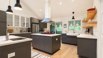 A modern kitchen with a central island, stainless steel appliances, and a view of greenery outside.