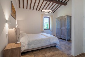 A bedroom with a bed, wooden floor, a wardrobe, a window, and a ceiling with exposed beams.