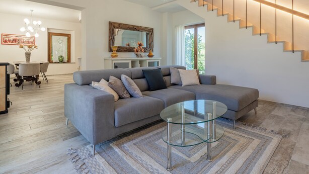 A modern living room with a grey sectional sofa, a glass coffee table, a staircase with wooden steps, and a large mirror above the fireplace. - Villetta Cafaggio Ac Panzano In Chianti (Castellina in Chianti)
