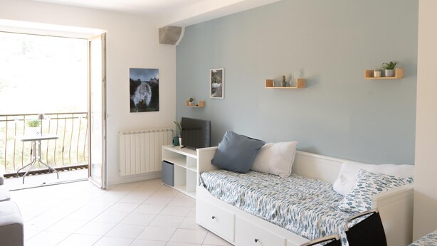 Ein Schlafzimmer mit Bett, Schreibtisch, Stuhl, Heizkörper und einem Balkon.