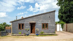 Une maison en bois à deux étages, avec une porte d’entrée, deux fenêtres et un petit porche agrémenté de plantes en pot.