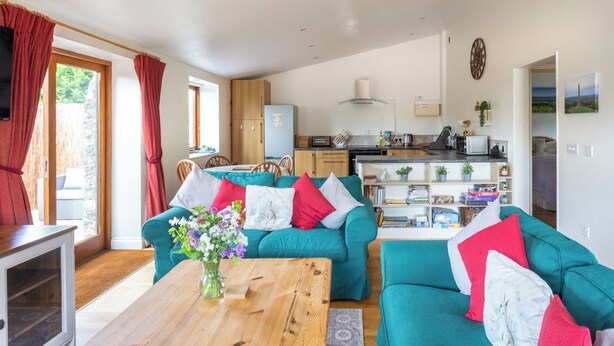Un salon moderne avec un canapé turquoise, une table basse en bois et un coin repas avec une cuisine en arrière-plan.