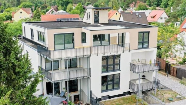 Un edifici residencial modern, de diverses plantes, amb balcons, grans finestres i un terrat pla.