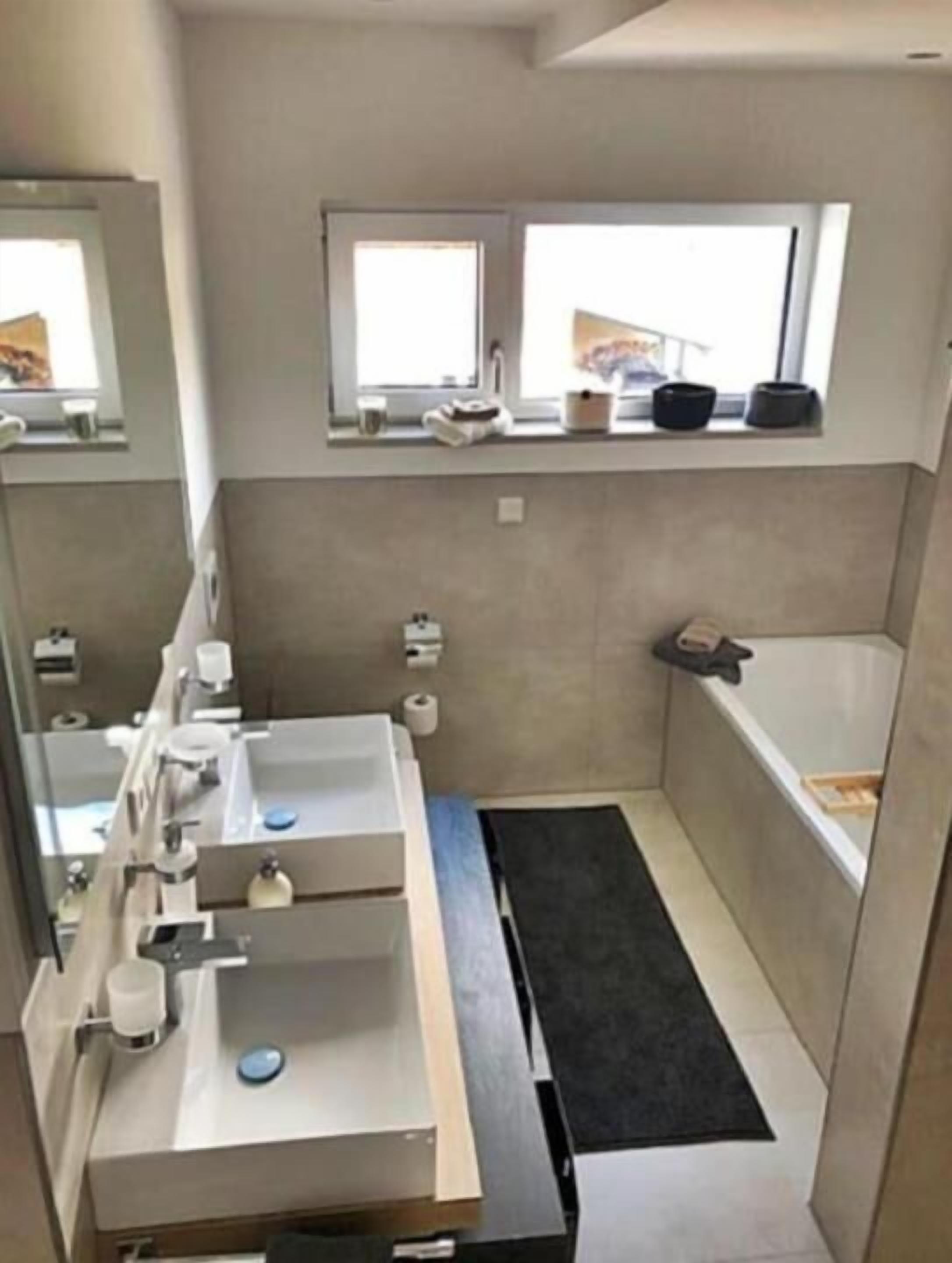 A modern bathroom with a large mirror, a sink, a toilet, and a window.