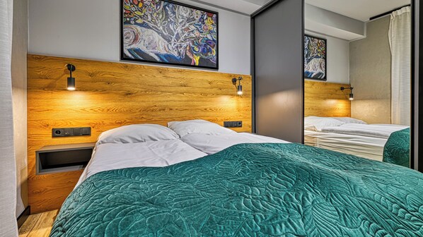 A modern hotel room with a wooden headboard, two beds with teal bedding, and artwork above the beds. - Apartamenty Sun & Snow Centrum Park (Szklarska Poreba)