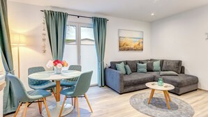 A modern living room with a grey sofa, a round dining table with blue chairs, and a small side table with a vase. - Haus Barnheide, Whg. Silbermöwe in Bansin - your retreat with balcony (Bansin)