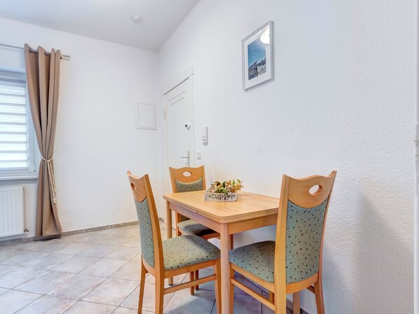 A dining area with a wooden table and four chairs, a small decorative plant, and a framed picture on the wall.