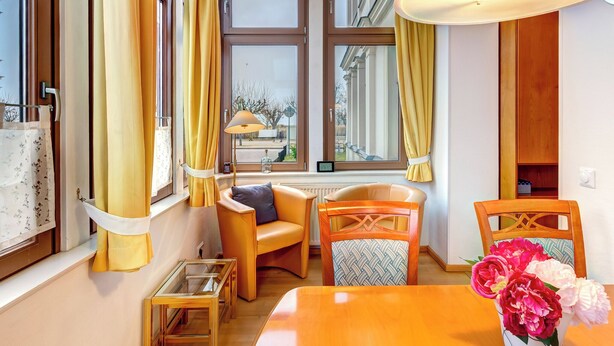 Una habitación de hotel moderna con una mesa de madera, dos sillas, una mesa de centro de vidrio y un jarrón con flores.