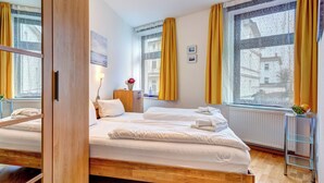 Un dormitorio moderno con una cama de madera, una mesita de noche pequeña con una lámpara y una ventana con cortinas amarillas.