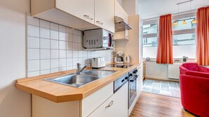 Una cocina moderna con microondas, tostadora y cafetera incorporadas. Hay un lavamanos con encimera de madera, y una silla roja en la zona de estar.