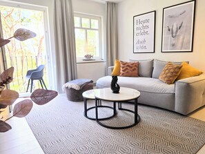 A living room with a sofa, a round coffee table, a chair, and a window with curtains. - Favorite suite on the beach in Ahlbeck: 50 m to the beach, up to 2 guests, WLAN (Ahlbeck (Seebad))