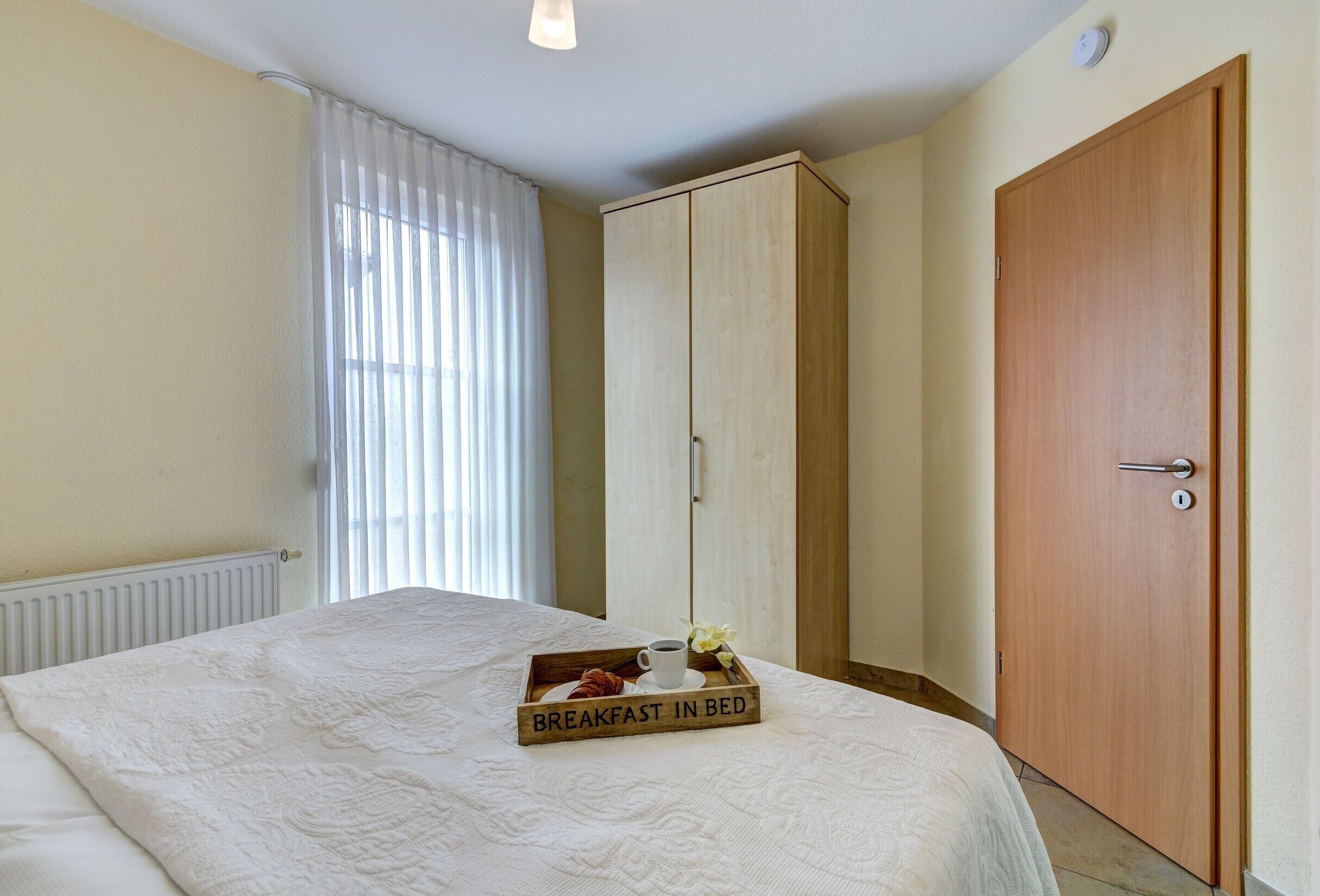Een slaapkamer met een bed, een houten kledingkast, een deur en een dienblad met ontbijtartikelen.