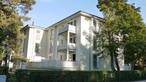 A multi-story residential building with balconies, a gated entrance, and a well-maintained hedge.