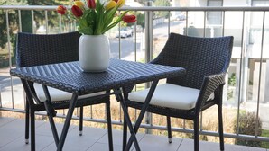 A balcony with wicker furniture, a white vase with tulips, and a view of a residential street.