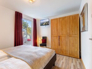 Ein Schlafzimmer mit einem Bett, einem Holzschrank, einem an der Wand befestigten Fernseher und einem Fenster mit Vorhängen.