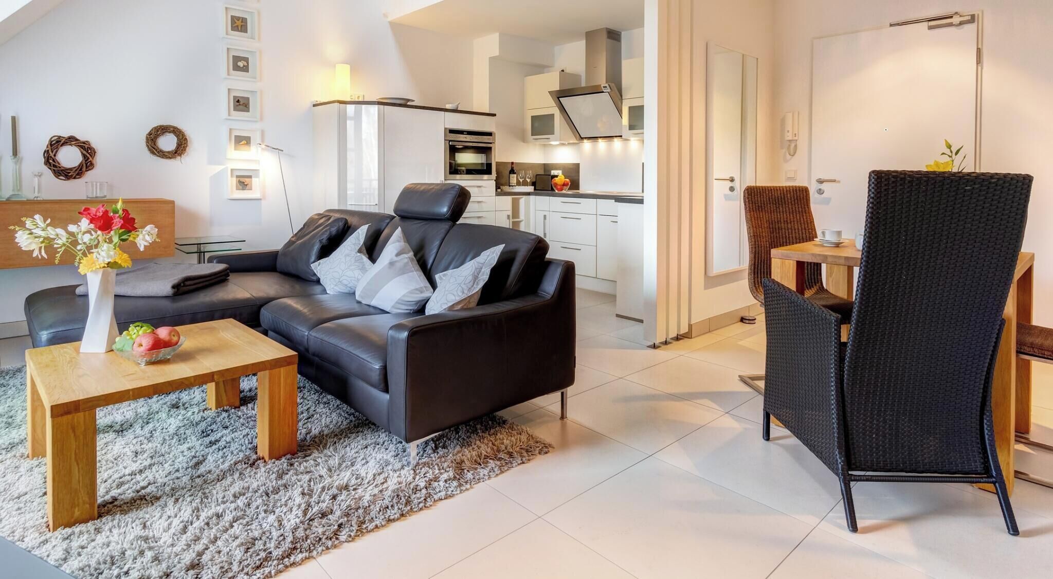 Un salon moderne avec un canapé en cuir noir, une table basse en bois et un fauteuil en osier noir.