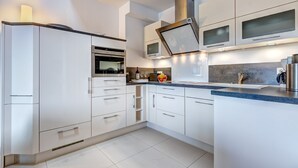 A modern kitchen with white cabinetry, a built-in oven, microwave, and a stainless steel range hood.