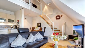 A modern living room with a black leather sofa, a wooden coffee table, and a TV. A staircase with a white railing leads to an upper level.