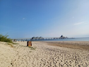 Una playa con un muelle que se adentra en el agua, con una zona cubierta y una estructura triangular al final.