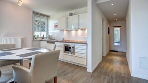 Une cuisine moderne avec des meubles blancs, un four encastré et un coin repas comprenant une table ronde et des chaises.