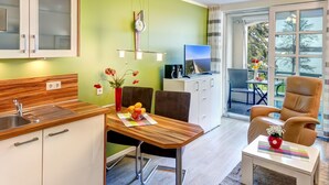 Et moderne køkken med træbordplade, spiseplads med bord og stole, en sofa og udsigt til det fri via et stort vindue.
