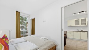 Un dormitorio con cama, ventana con cortinas, mesita de noche y vistas a una zona de cocina.