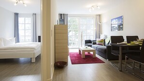 Una sala moderna con cama, sofá, mesa de comedor y un ventanal grande.