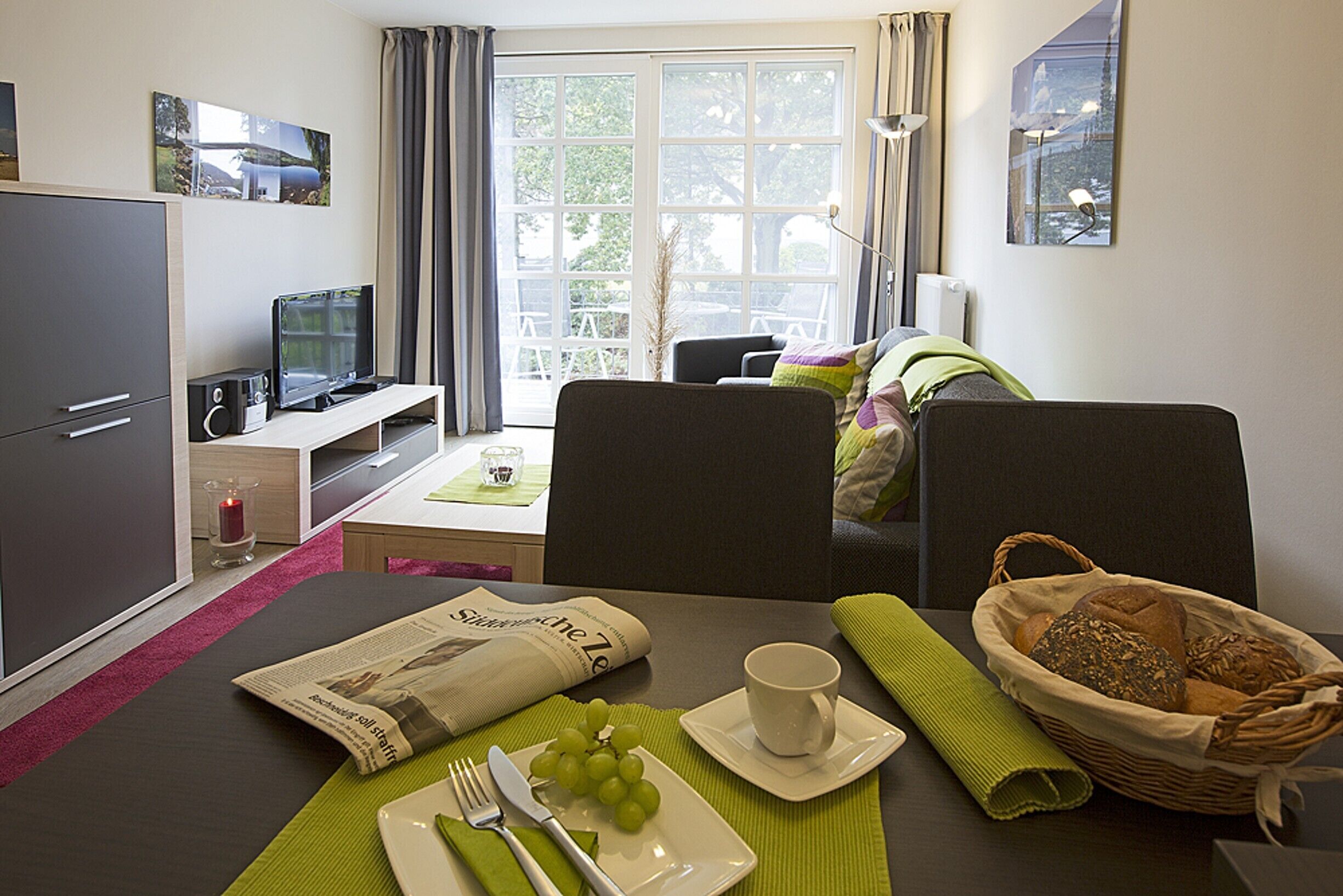 Et hotelværelse med spiseplads, fjernsyn, skrivebord og et vindue med gardiner.